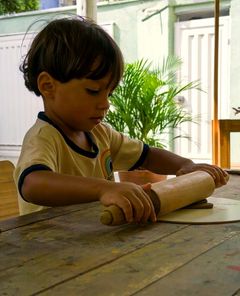 Menino abrindo massinha com um rolo de madeira