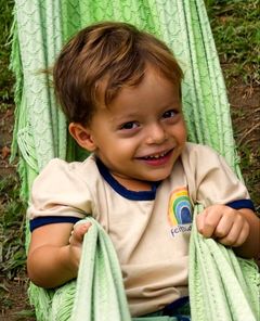 Menino sorrindo deitado numa rede no quintal