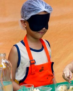 Criança de olhos vendados provando alimentos na aula de culinária