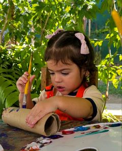Menina de avental pintando um rolo de papelão com pincel
