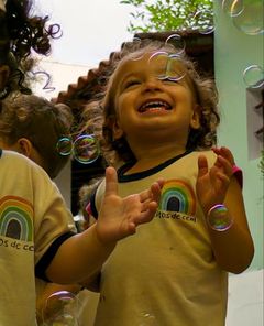 Menina pequena rindo e batendo palmas entre bolhas de sabão