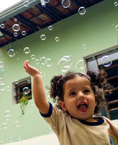 Menina rindo e tentando pegar bolhas de sabão