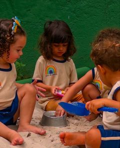 Crianças pequenas brincando no tanque de areia com baldinho e pá