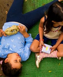 Meninas deitadas na grama brincando com um crânio de dinossauro de brinquedo