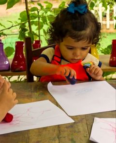 Menina pequena desenhando com giz de cera na mesa do quintal