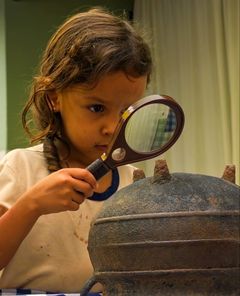 Menina examinando um objeto antigo de ferro com uma lupa