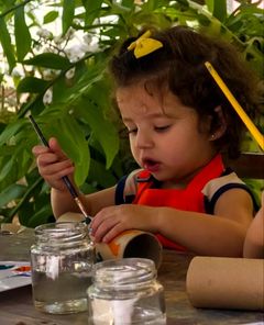 Menina de avental pintando um rolo de papelão no ateliê do jardim