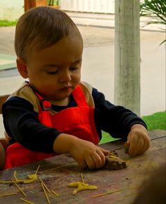 Bebê de avental modelando massa com macarrão na mesa
