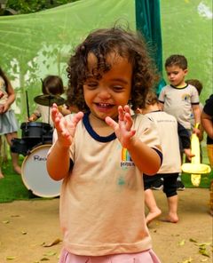Menina sorrindo e batendo palmas no quintal durante o Rock Kids