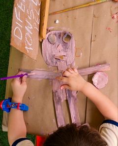 Criança pintando um boneco de papelão vista de cima