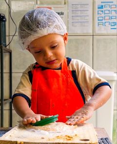 Menino de touca e avental amassando massa na tábua da cozinha