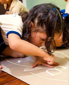 Menina desenhando com giz no papel pardo estendido no chão