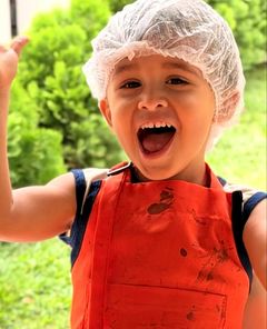 Menino de touca e avental sorrindo na aula de culinária
