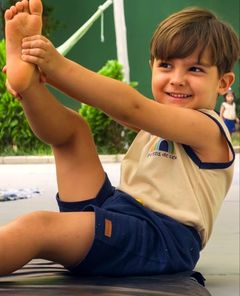 Menino sorrindo e alongando a perna na aula de yoga