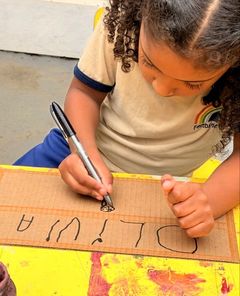 Menina escrevendo o próprio nome num papelão com caneta