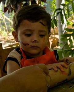 Bebê de avental com o rosto pintado de tinta numa atividade de pintura