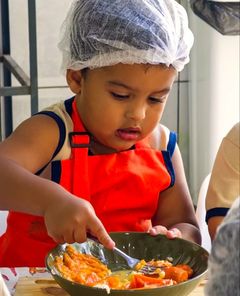 Menino de touca e avental amassando legumes com o garfo na aula de culinária