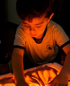 Menino desenhando com os dedos na areia da mesa de luz